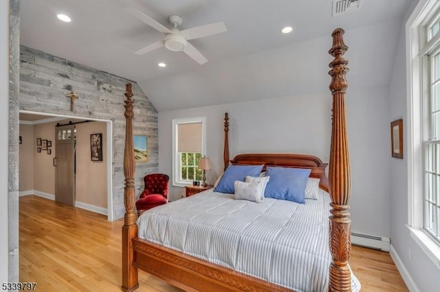 bedroom featuring lofted ceiling, a barn door, baseboard heating, and wood finished floors