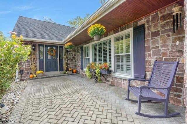 property entrance with covered porch, stone siding, and roof with shingles