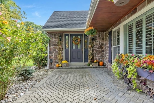 doorway to property featuring stone siding and roof with shingles