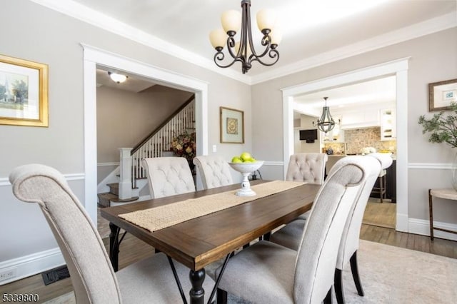 dining room with crown molding, an inviting chandelier, wood finished floors, baseboards, and stairs