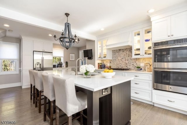 kitchen featuring stainless steel appliances, decorative backsplash, a sink, an island with sink, and a kitchen breakfast bar