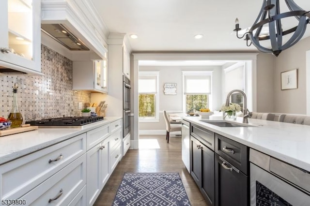 kitchen with stainless steel appliances, premium range hood, a sink, white cabinetry, and decorative backsplash