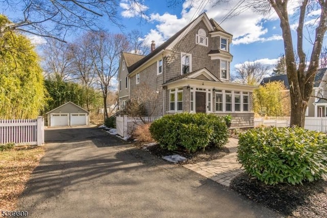 view of front of house featuring a garage, a sunroom, a chimney, fence, and an outdoor structure