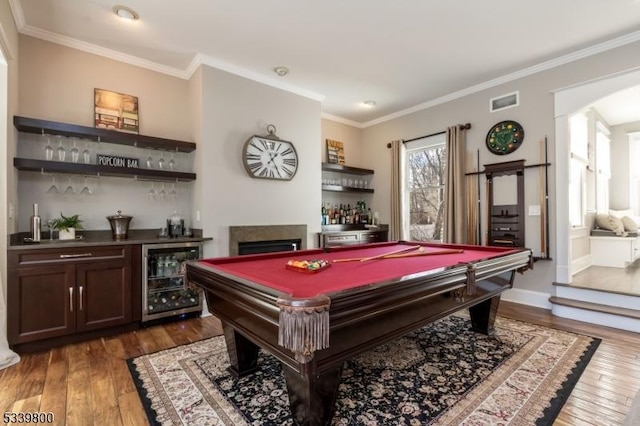 rec room featuring beverage cooler, arched walkways, hardwood / wood-style flooring, ornamental molding, and a bar