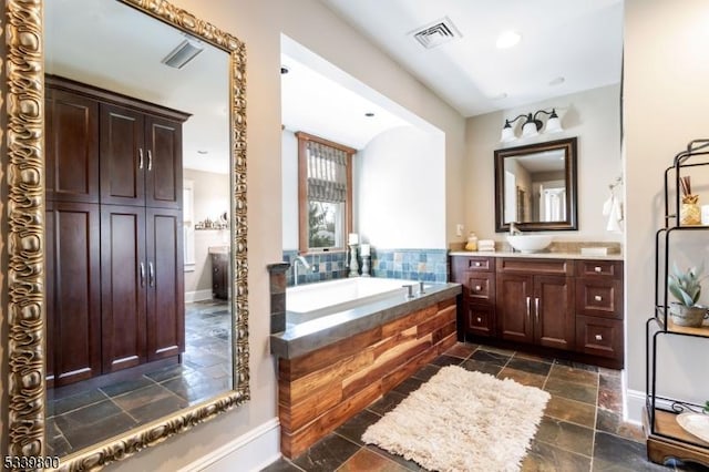 bathroom featuring stone tile floors, baseboards, visible vents, vanity, and a bath