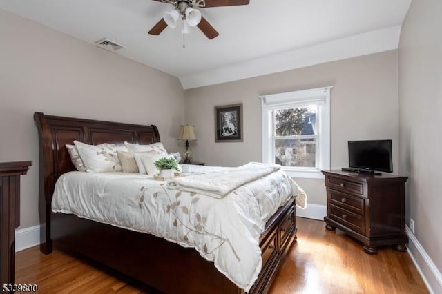 bedroom with ceiling fan, wood finished floors, visible vents, baseboards, and vaulted ceiling