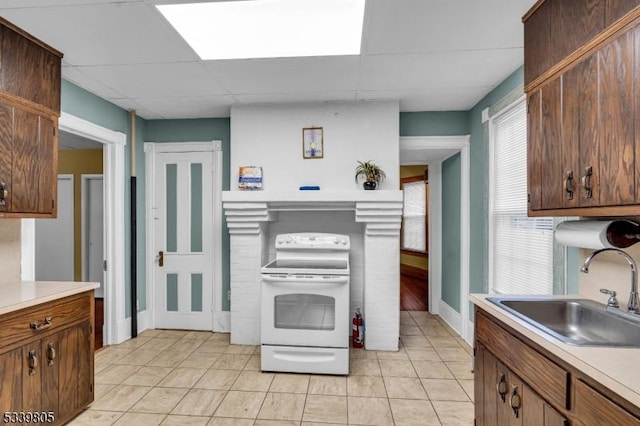 kitchen featuring light tile patterned floors, electric stove, light countertops, a paneled ceiling, and a sink