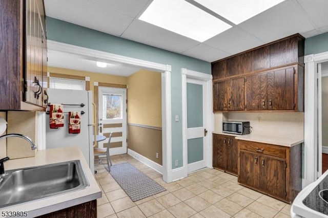 kitchen with a drop ceiling, stainless steel microwave, light countertops, and a sink