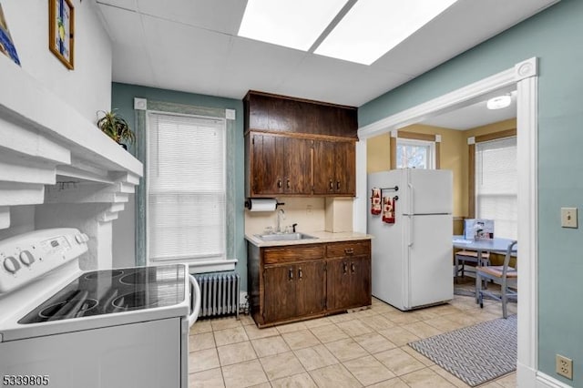 kitchen with radiator, white appliances, a sink, and dark brown cabinetry