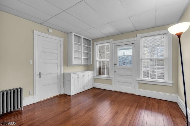 spare room with a paneled ceiling, dark wood-style floors, radiator heating unit, and baseboards