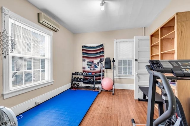 exercise room featuring light wood finished floors, baseboards, and a wall mounted air conditioner