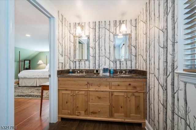 full bathroom with double vanity, wallpapered walls, ensuite bath, wood finished floors, and a sink