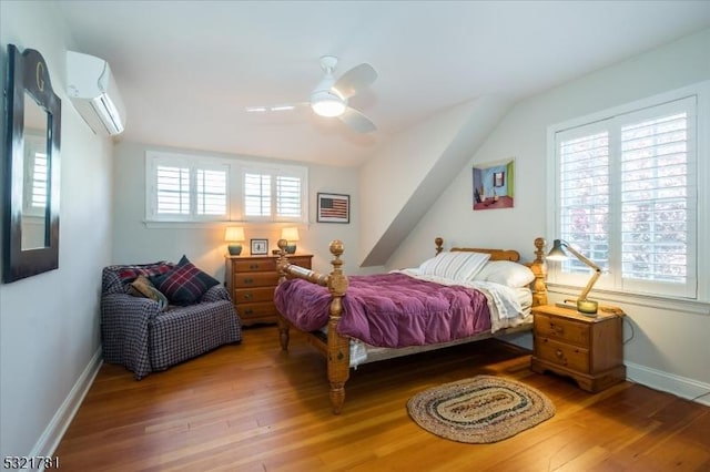 bedroom featuring an AC wall unit, vaulted ceiling, baseboards, and wood finished floors