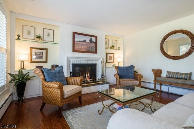 living room with dark wood-style floors, a brick fireplace, a baseboard heating unit, and built in shelves