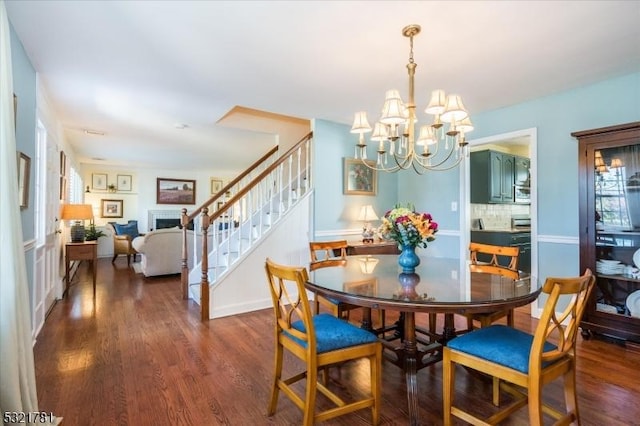 dining space featuring a chandelier, dark wood-style flooring, a fireplace, baseboards, and stairs