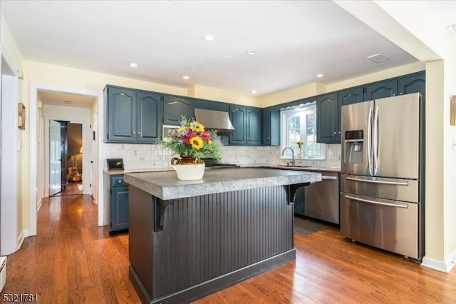 kitchen with blue cabinets, wood finished floors, a sink, appliances with stainless steel finishes, and a center island