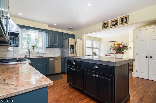 kitchen featuring dark wood-style floors, a center island, blue cabinetry, stainless steel appliances, and a sink