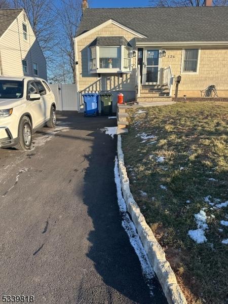 view of front of house with aphalt driveway, a shingled roof, brick siding, fence, and a chimney