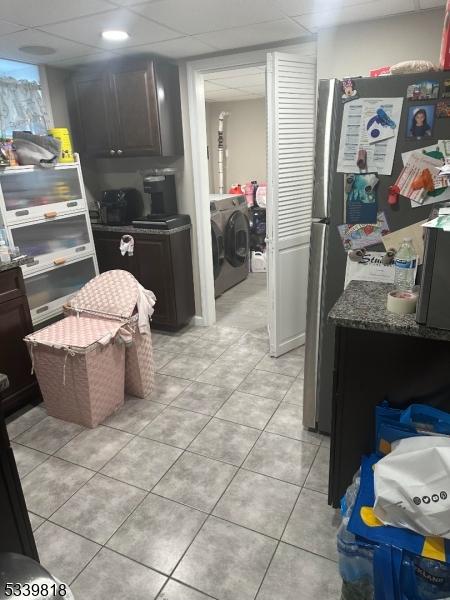 kitchen with stone countertops, a drop ceiling, freestanding refrigerator, washing machine and dryer, and light tile patterned flooring