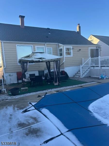 rear view of house featuring a patio, a chimney, a gazebo, a covered pool, and a wooden deck