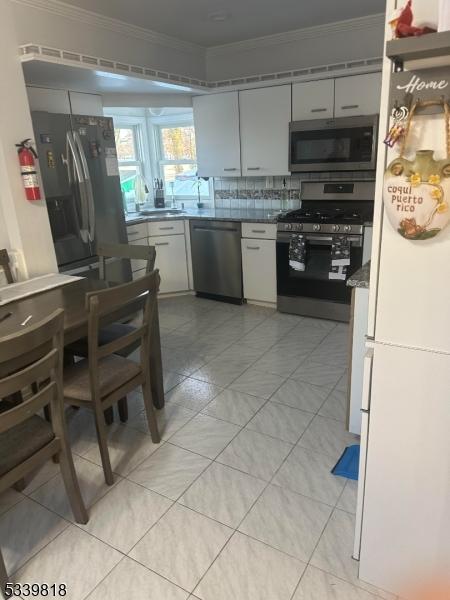 kitchen featuring stainless steel appliances, tasteful backsplash, a sink, and crown molding