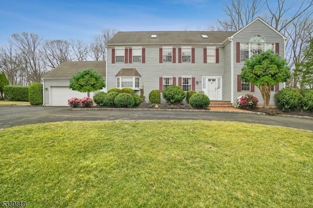 colonial house featuring a front lawn, an attached garage, and aphalt driveway