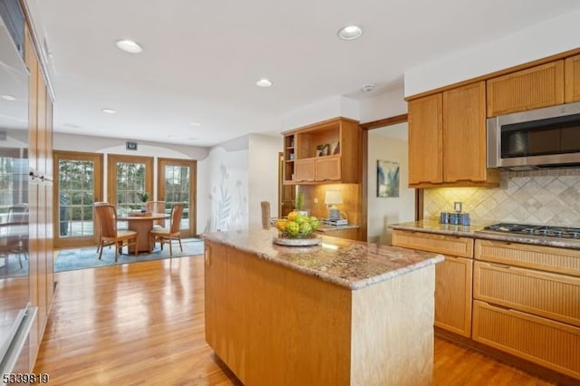 kitchen with light stone counters, a kitchen island, appliances with stainless steel finishes, light wood-type flooring, and backsplash