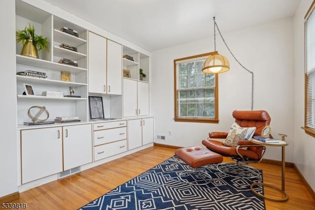 living area with light wood finished floors, visible vents, and baseboards