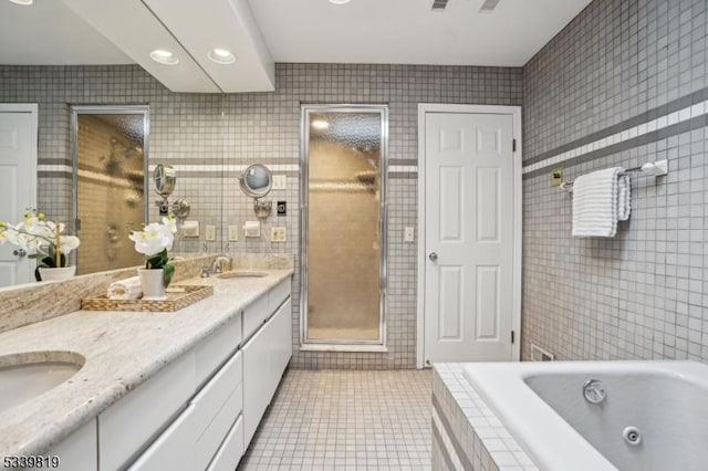 bathroom featuring double vanity, tile walls, a tub with jets, tile patterned floors, and a sink