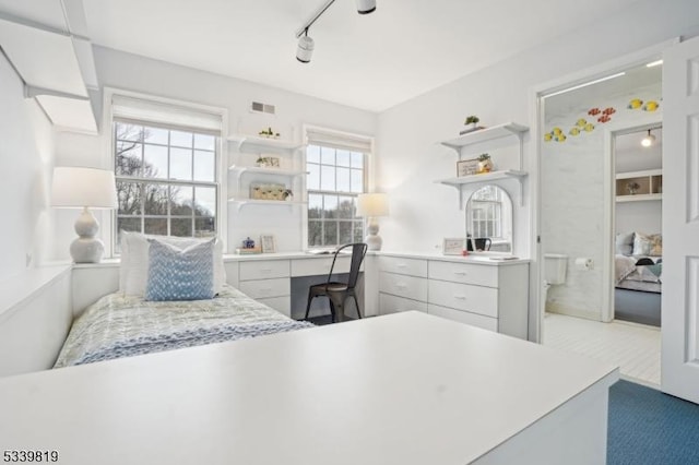 bedroom with built in desk, visible vents, and track lighting