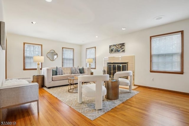 living area with a glass covered fireplace, baseboards, light wood finished floors, and recessed lighting