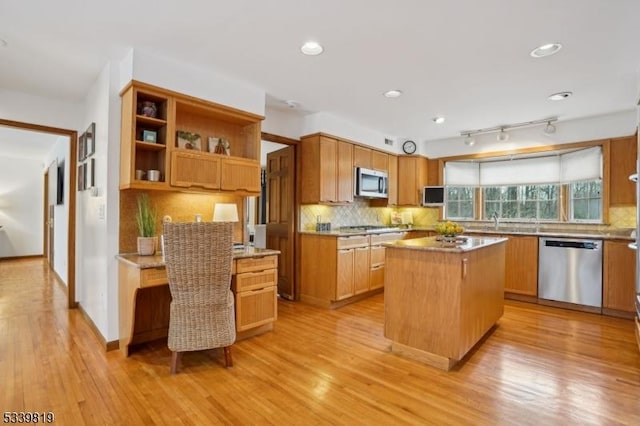 kitchen featuring a center island, light wood finished floors, stainless steel appliances, light countertops, and decorative backsplash