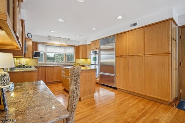 kitchen with light stone counters, visible vents, appliances with stainless steel finishes, brown cabinetry, and a kitchen island