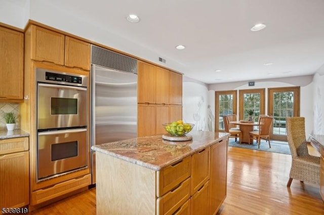 kitchen featuring light wood finished floors, appliances with stainless steel finishes, light stone countertops, and a center island