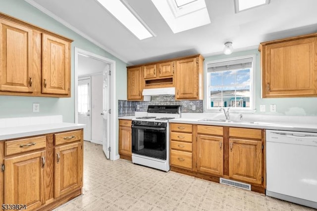 kitchen with vaulted ceiling with skylight, under cabinet range hood, white appliances, a sink, and visible vents