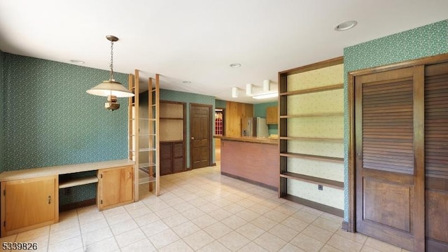 interior space with open shelves, wallpapered walls, stainless steel refrigerator with ice dispenser, built in desk, and hanging light fixtures