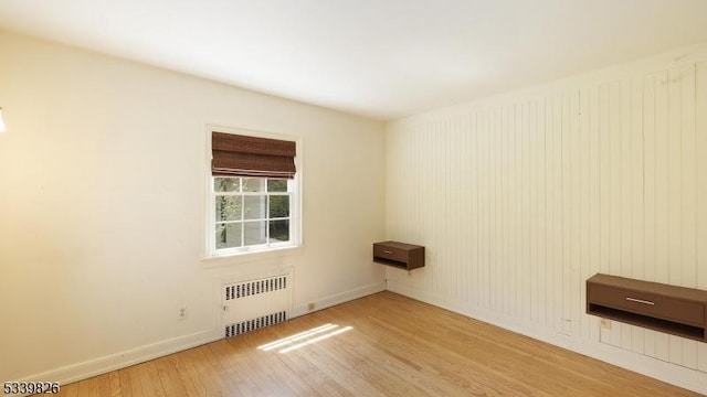 unfurnished room featuring baseboards, radiator, and wood finished floors