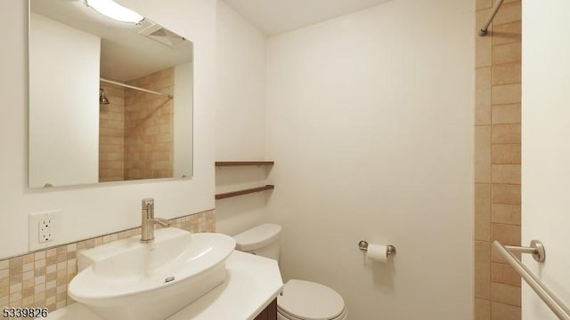 bathroom featuring vanity, toilet, tiled shower, and visible vents