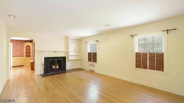 unfurnished living room featuring a fireplace with flush hearth, wood finished floors, baseboards, recessed lighting, and arched walkways