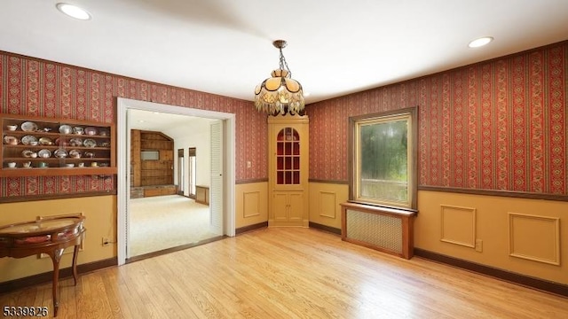 unfurnished dining area with wallpapered walls, a chandelier, wainscoting, and wood finished floors