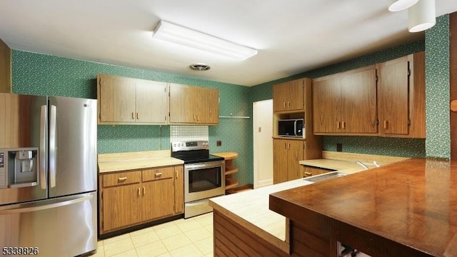 kitchen featuring appliances with stainless steel finishes, tasteful backsplash, light countertops, a sink, and wallpapered walls