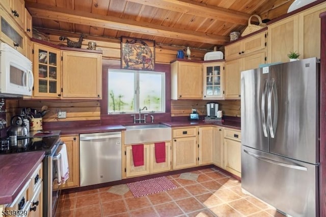 kitchen with stainless steel appliances, dark countertops, a sink, and beamed ceiling