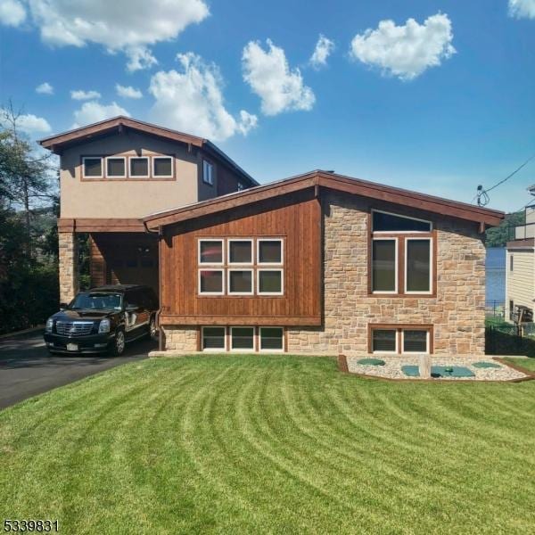 back of property with driveway, stone siding, and a yard