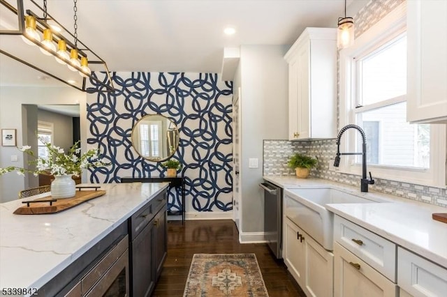 kitchen with a sink, stainless steel dishwasher, white cabinets, baseboards, and dark wood-style flooring