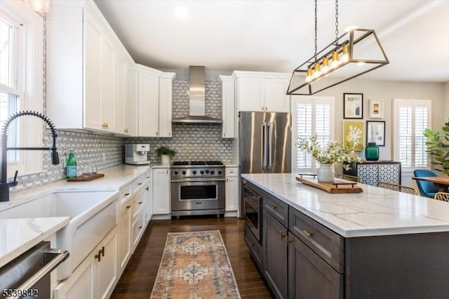 kitchen featuring a sink, tasteful backsplash, white cabinetry, wall chimney exhaust hood, and high end appliances