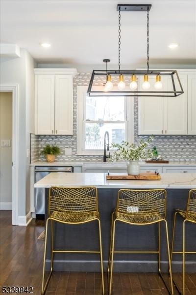 kitchen with a kitchen bar, stainless steel dishwasher, and white cabinetry