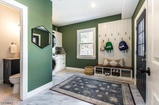 mudroom with stacked washer / dryer, marble finish floor, and baseboards