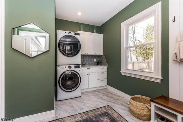 laundry area featuring baseboards, stacked washer / drying machine, cabinet space, and marble finish floor