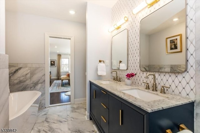 bathroom with a soaking tub, double vanity, marble finish floor, and a sink