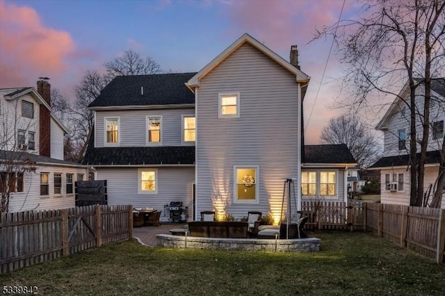 back of property at dusk featuring a fenced backyard, a lawn, a fire pit, and a patio